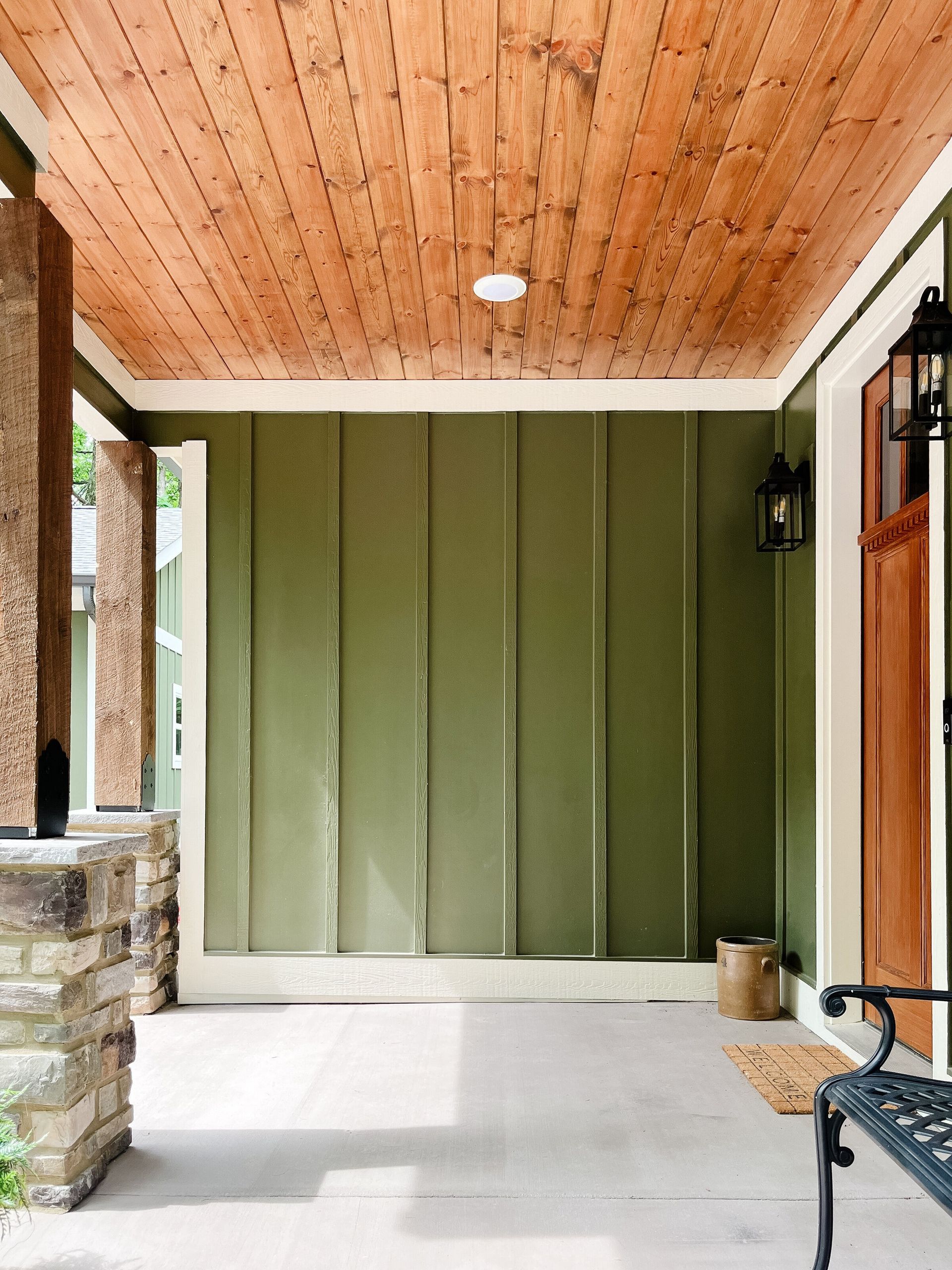 Olive green porch with a wooden ceiling, white trim, and stone columns.