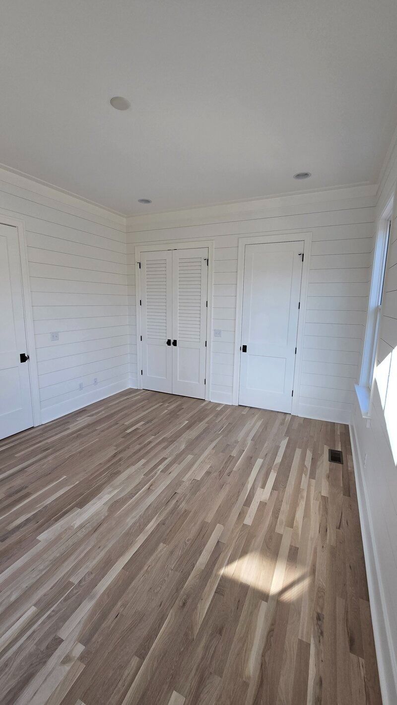 Empty room with light wood floor, white paneled walls and doors, and black door handles.