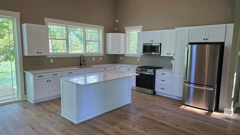 Modern kitchen with white cabinets, stainless steel appliances, and island. Natural light floods the space.