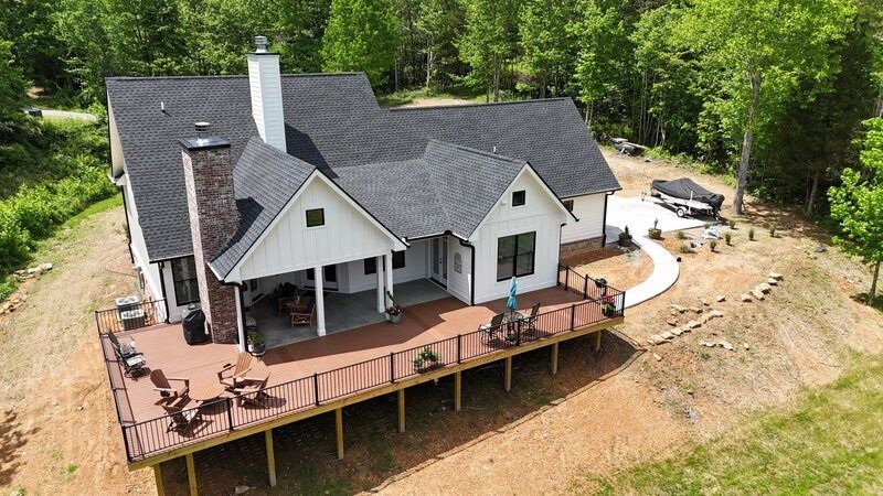 Drone view of a white and black farmhouse with a large deck and chimney.