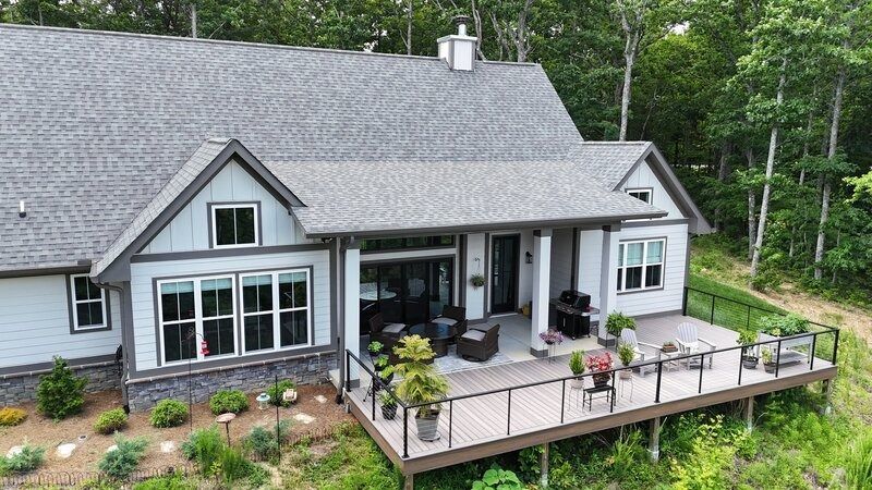 Gray house with deck and forest backdrop.