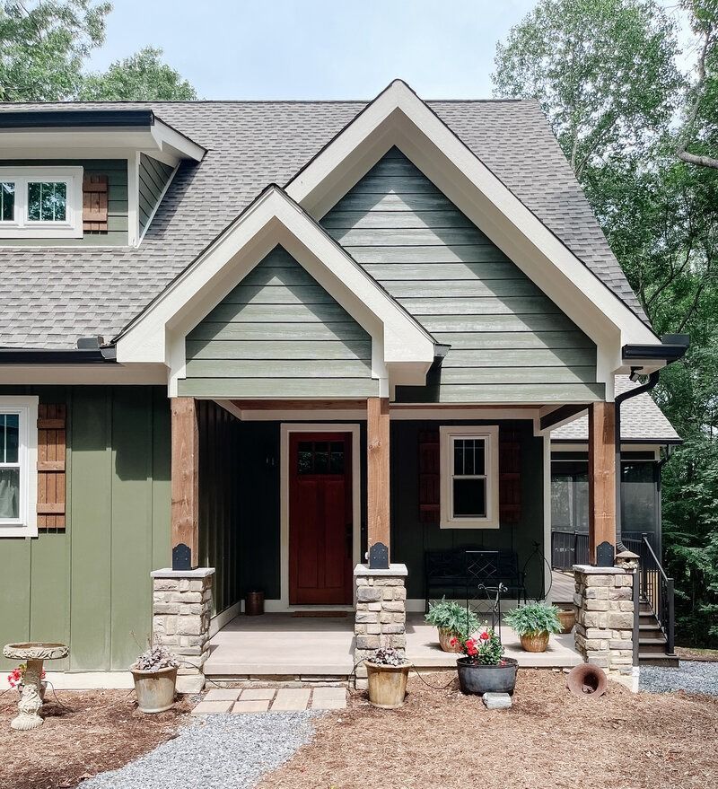 Green house with red door, stone pillars, and brown shutters.
