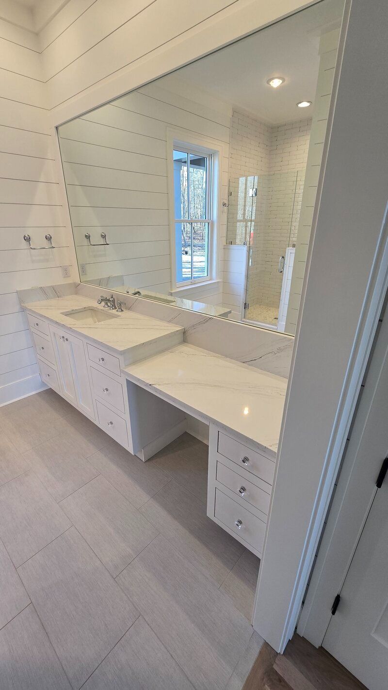 White vanity with mirror in a bright bathroom with wood-look flooring and a window in the background.