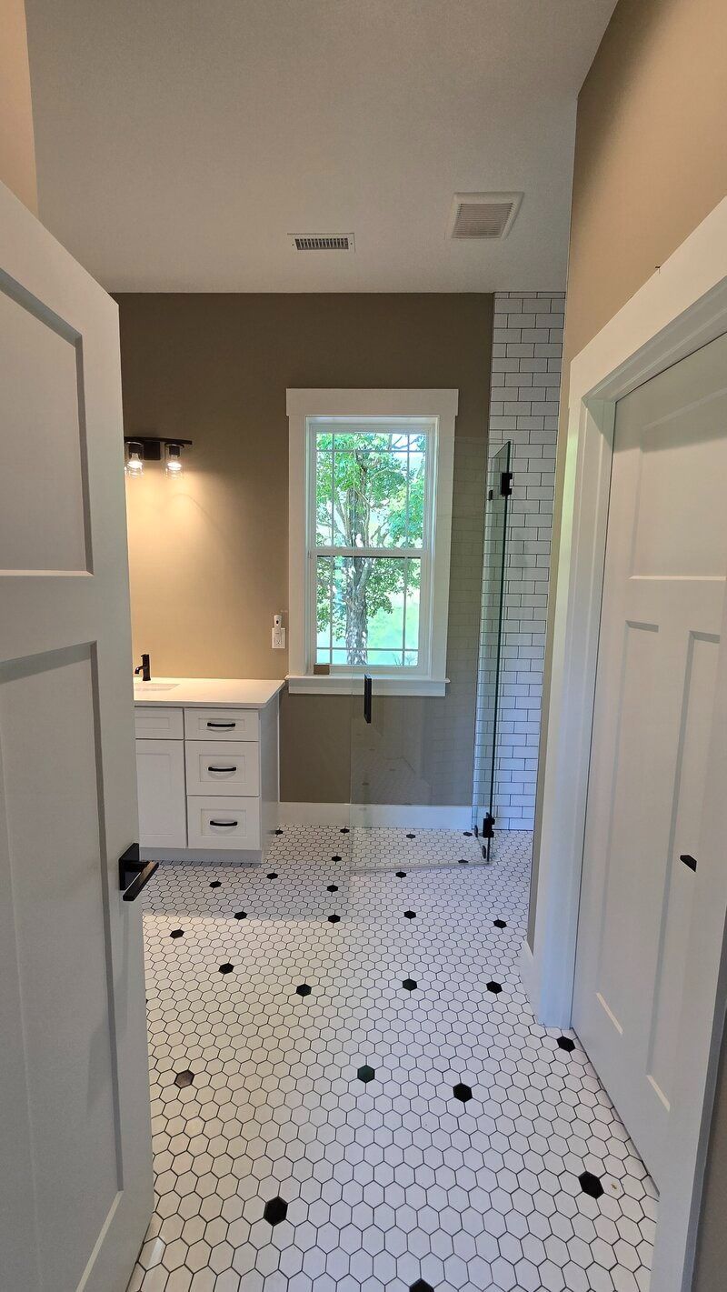 Bathroom with white and black patterned floor, white cabinets, and a window.
