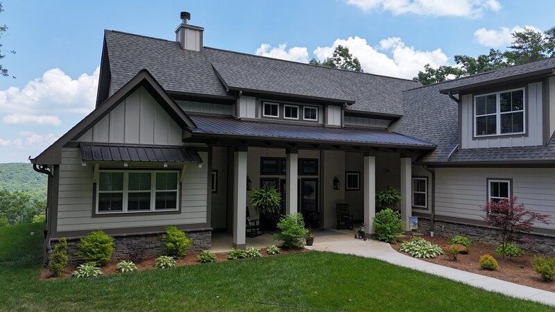 Exterior view of a beige and gray house with columns, a covered porch, and landscaped yard.