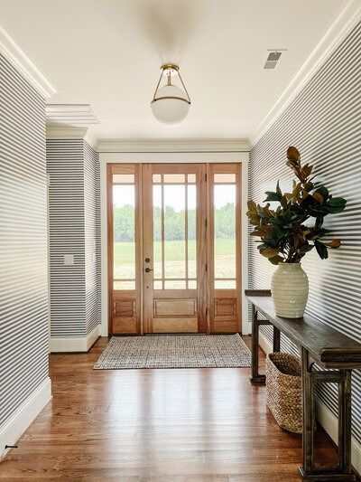 Entryway with striped wallpaper, hardwood floor, wooden console, and door leading to a green outdoor view.
