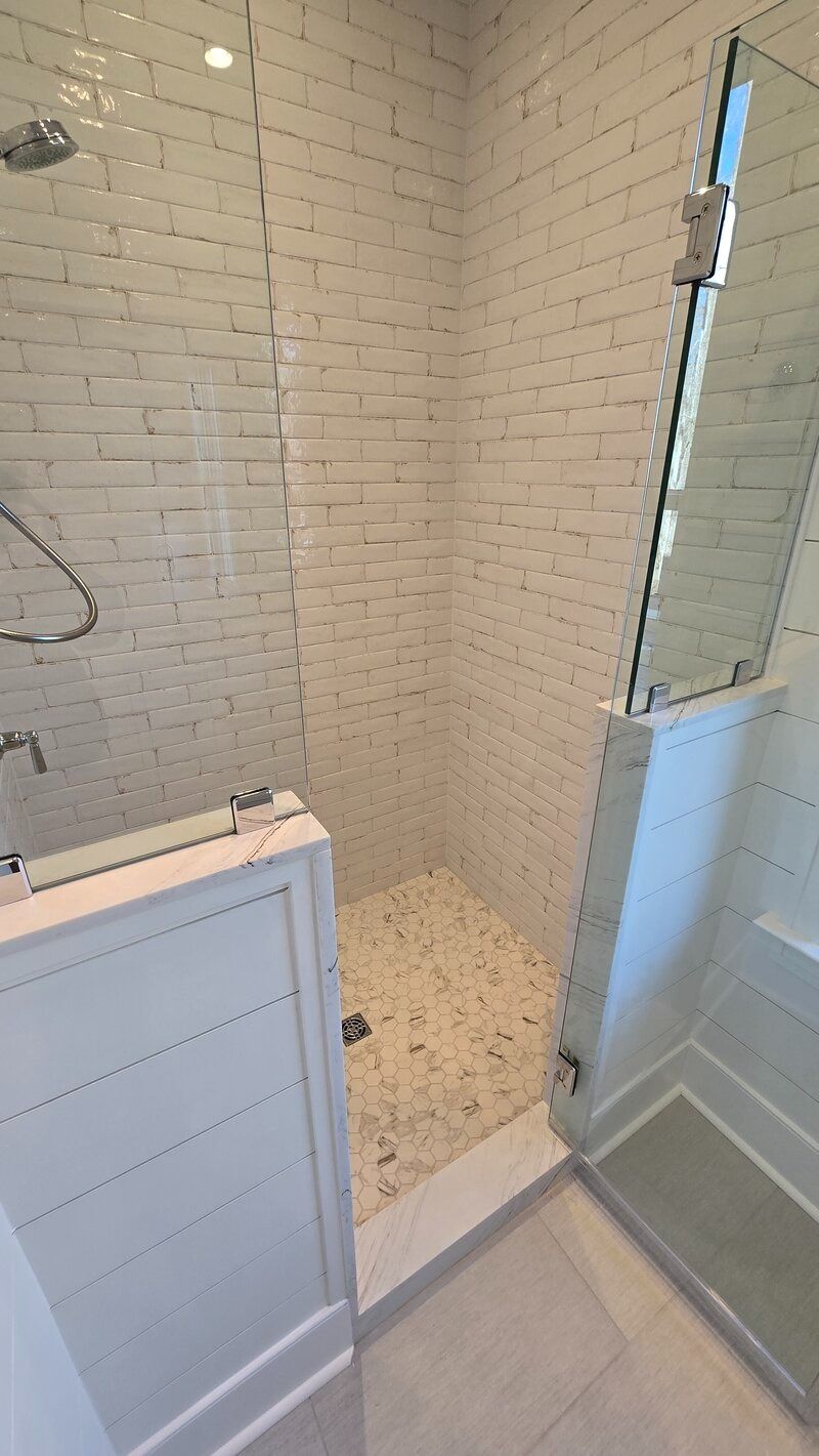 White tiled walk-in shower with glass doors, stone floor, and white trim.