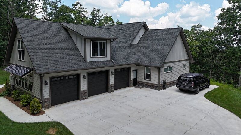 Modern house with a three-car garage, grey roof, and a black van parked in the driveway.