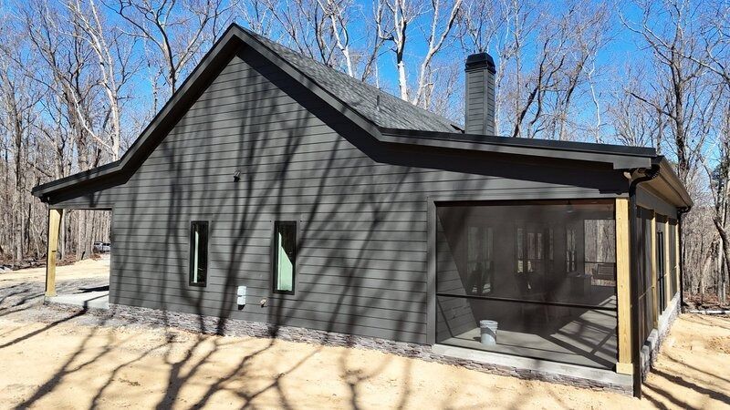 Dark gray cabin with a screened porch, chimney, and bare trees.