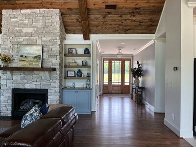 Living room with stone fireplace, wooden ceiling, built-in shelves, and entryway with double doors.