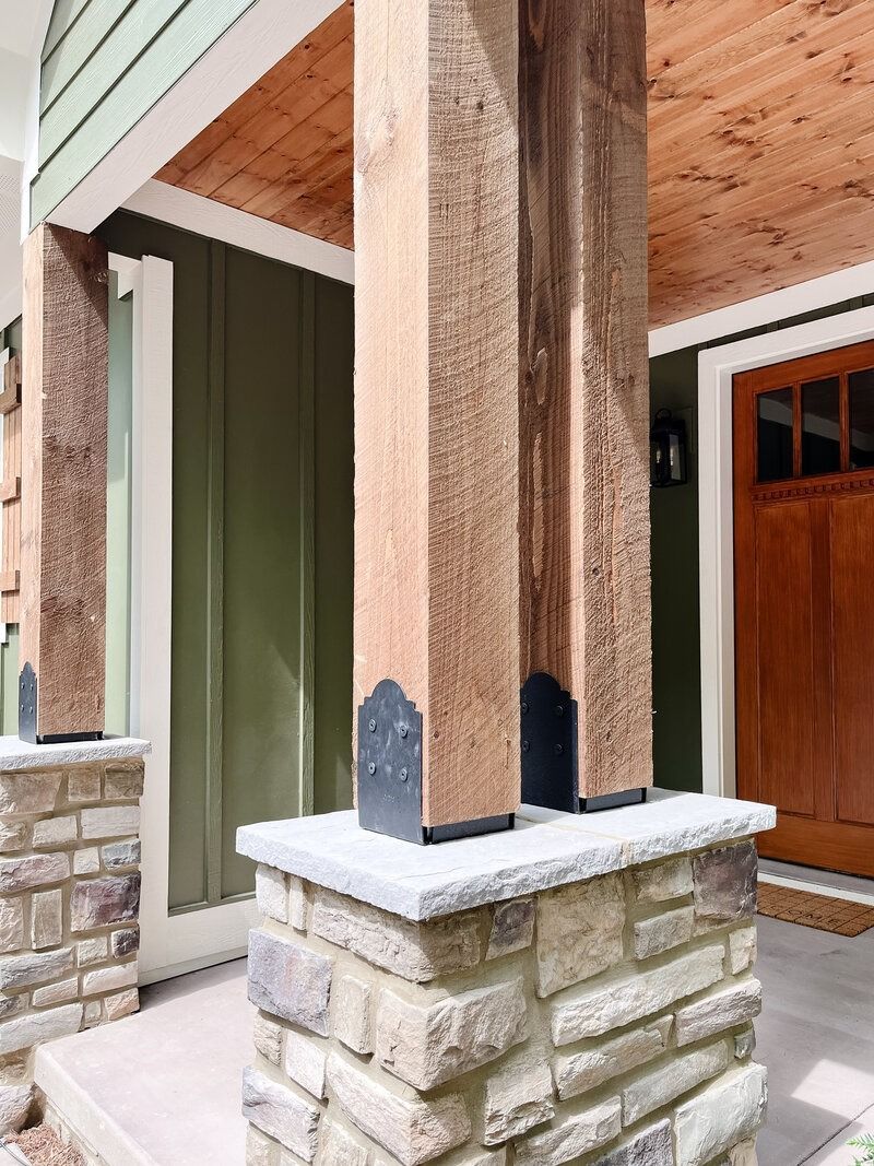 Stone and wood porch columns supporting a wooden ceiling and entrance door.