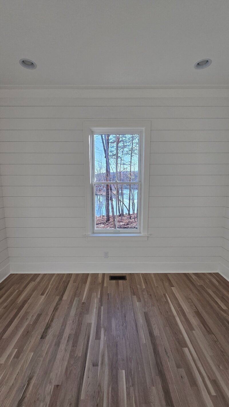 Empty room with white horizontal paneling, window, hardwood floors, and recessed lighting.