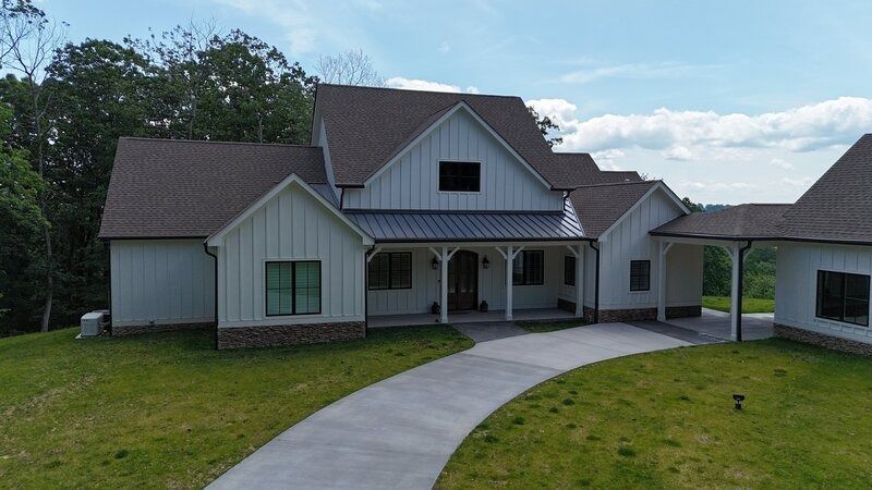 White farmhouse with a long driveway on a sunny day.