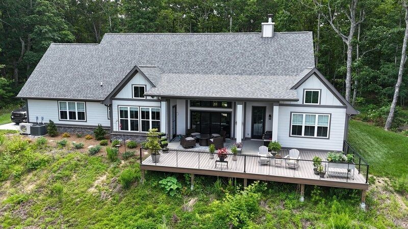 Gray house with a deck overlooking a hillside, surrounded by trees.