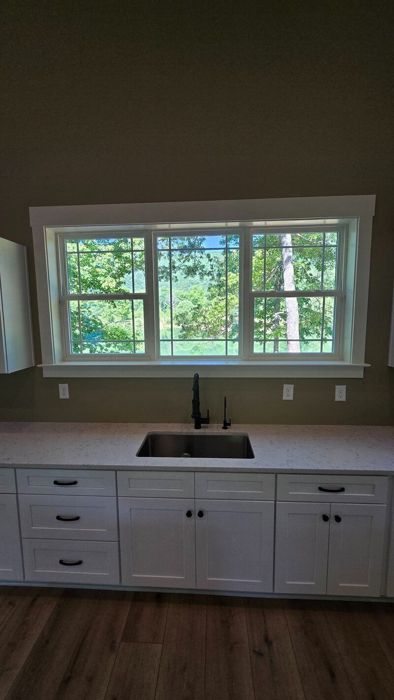 Kitchen with white cabinets, stainless sink, and window overlooking trees.