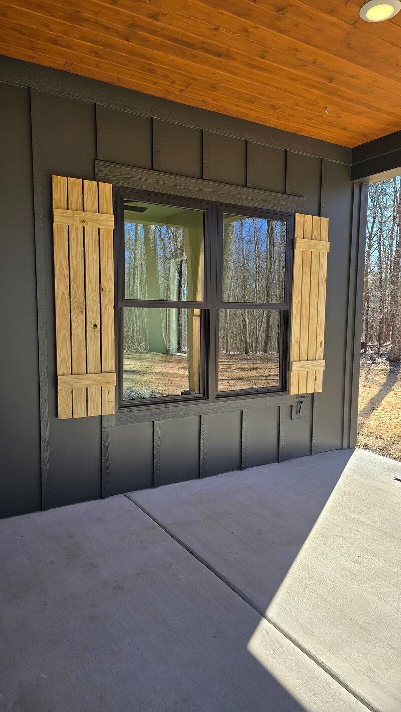 Window with wooden shutters on a dark gray wall, viewed from a concrete patio.