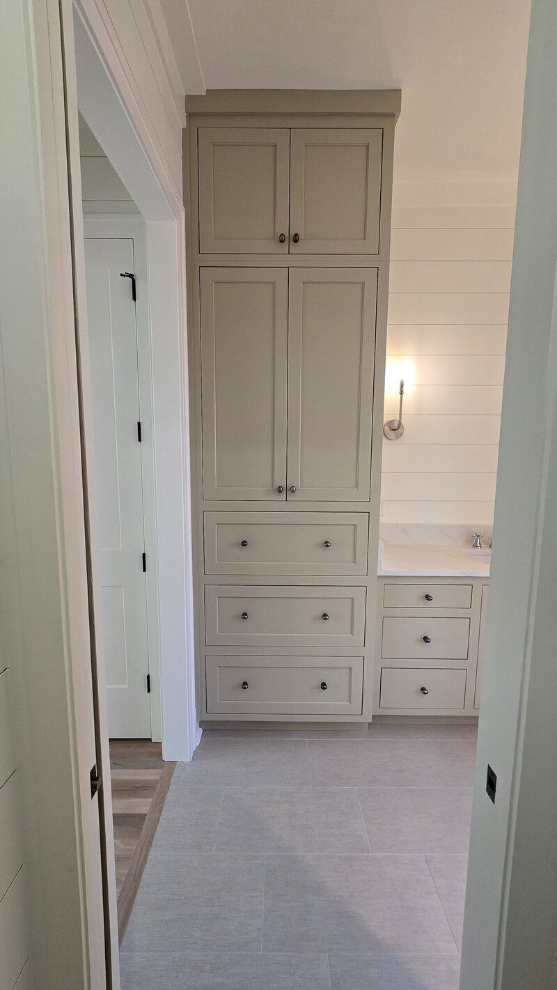 Tall, light-colored cabinet with drawers and doors in a hallway with a smaller cabinet and sconce.