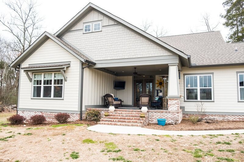 Beige house with a covered porch. Red brick steps lead to seating area.