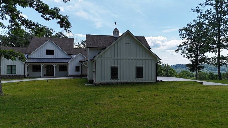 White farmhouse with a large yard, set against a backdrop of trees and a blue sky.