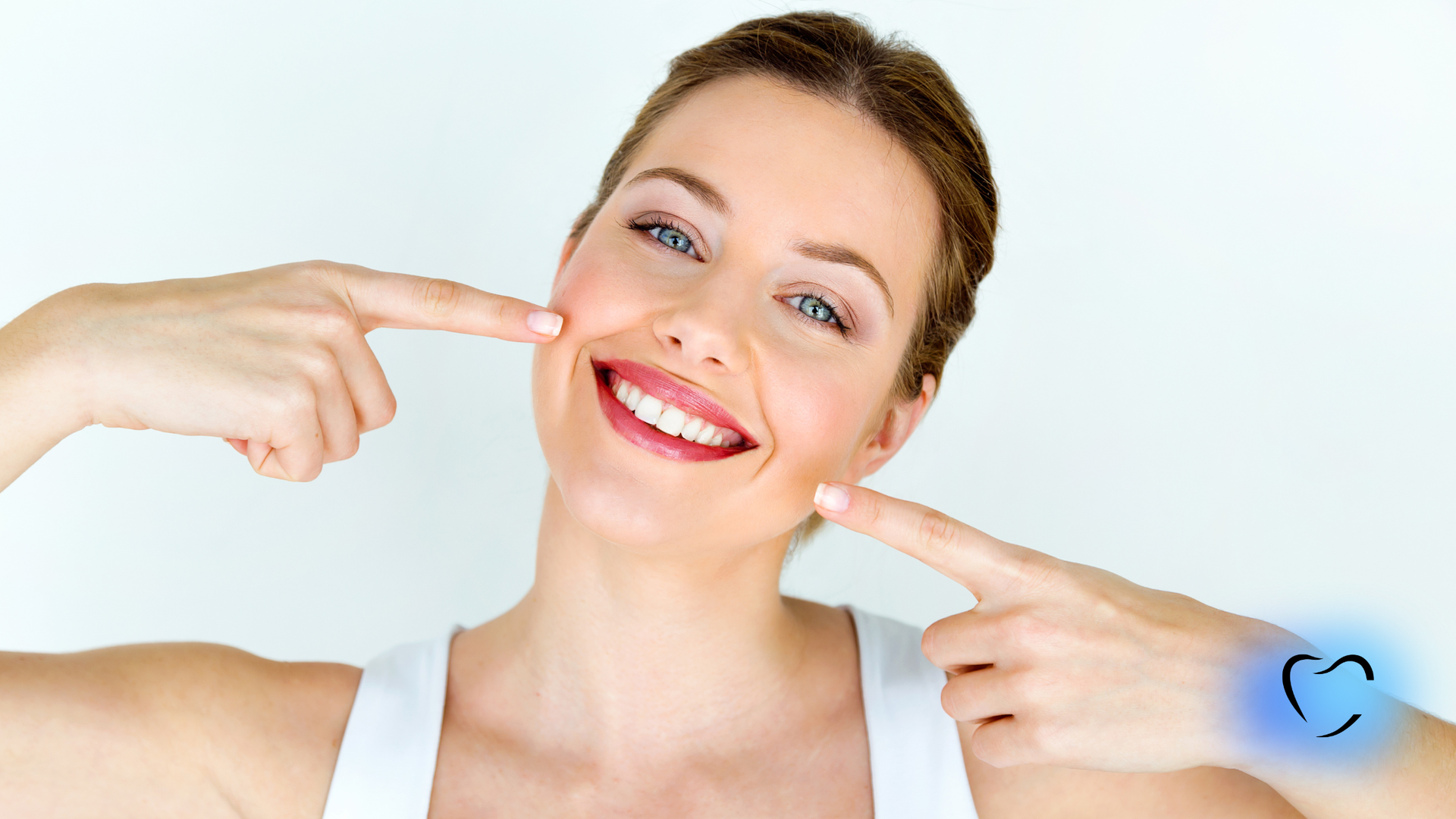 Woman smiling, pointing to her cheeks. White tank top, light background, blue light heart icon.