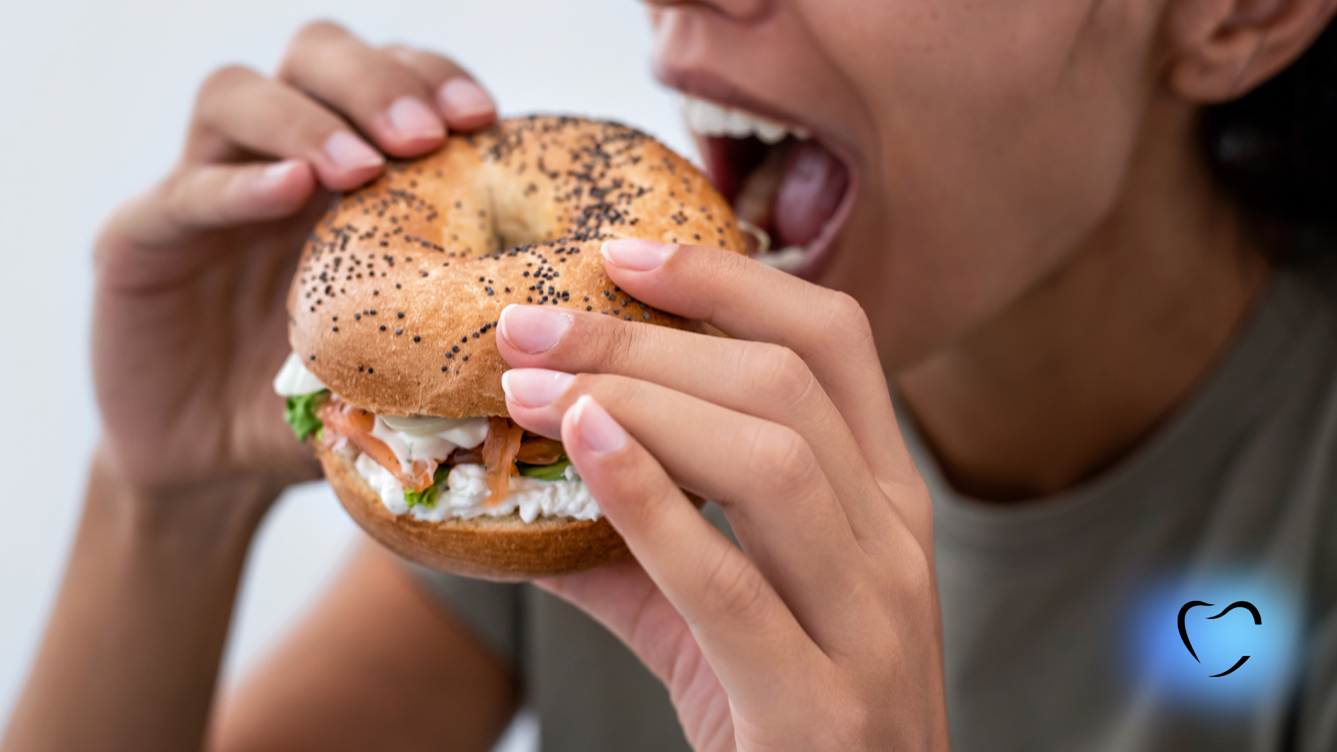 Person taking a bite from an everything bagel with cream cheese and lox.