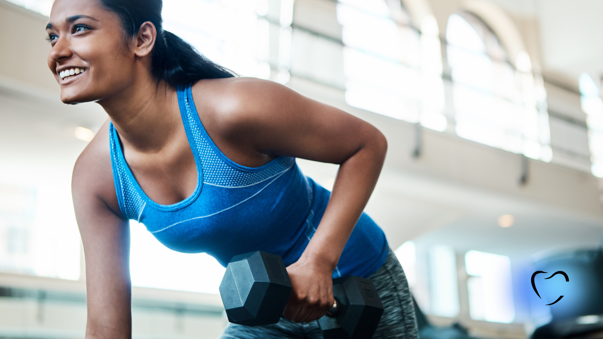 Woman in blue tank top lifting dumbbell in a gym. Smiling with a focused expression.