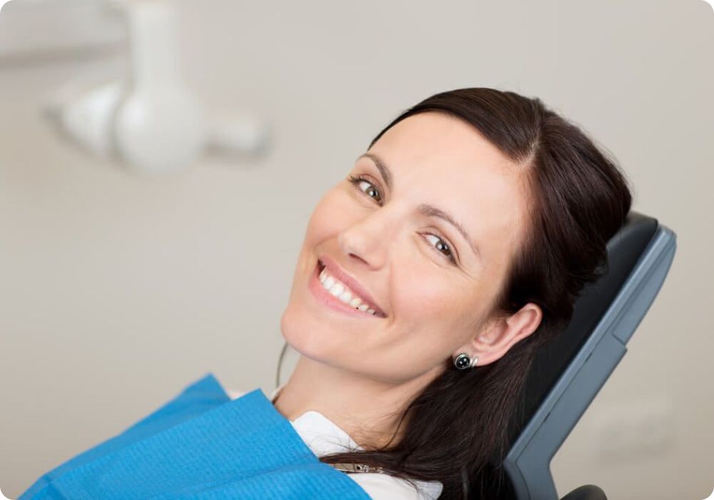 A woman is smiling while sitting in a dental chair.