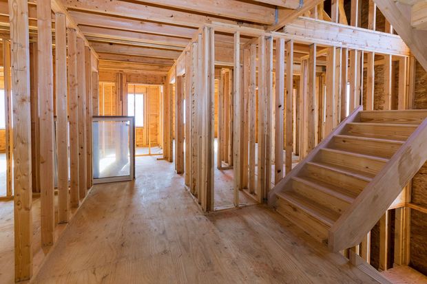Unfinished wooden house interior with framing, stairs, and a bright doorway at the end