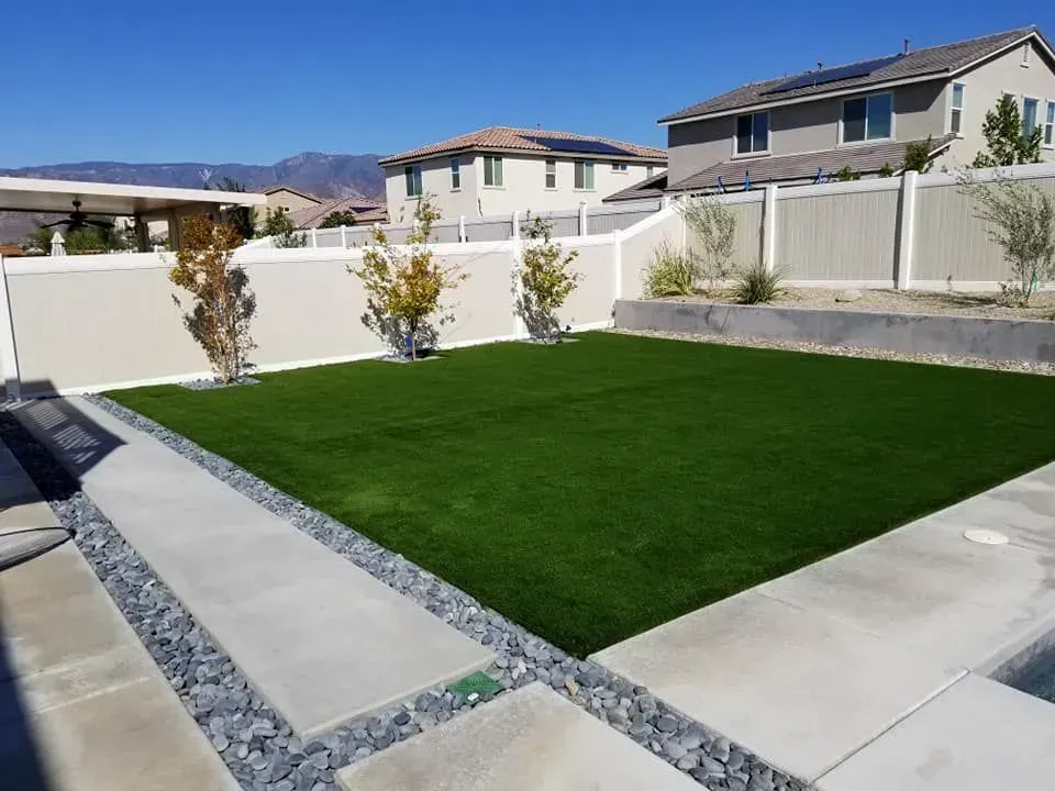 A backyard with a large lawn and a white fence.