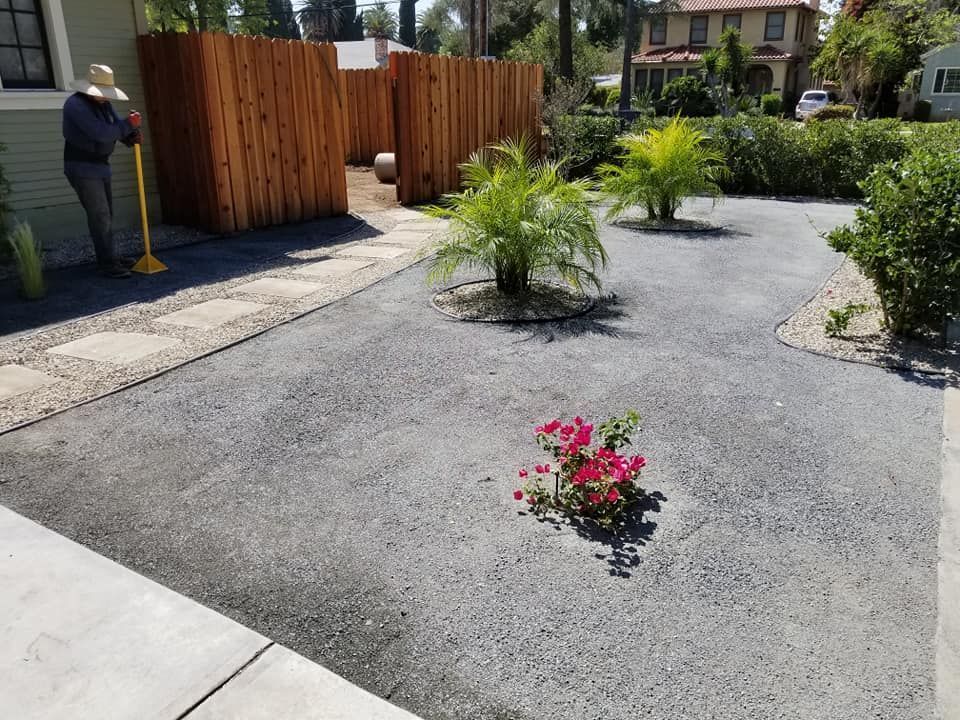 A man with a broom is standing in a driveway next to a fence.