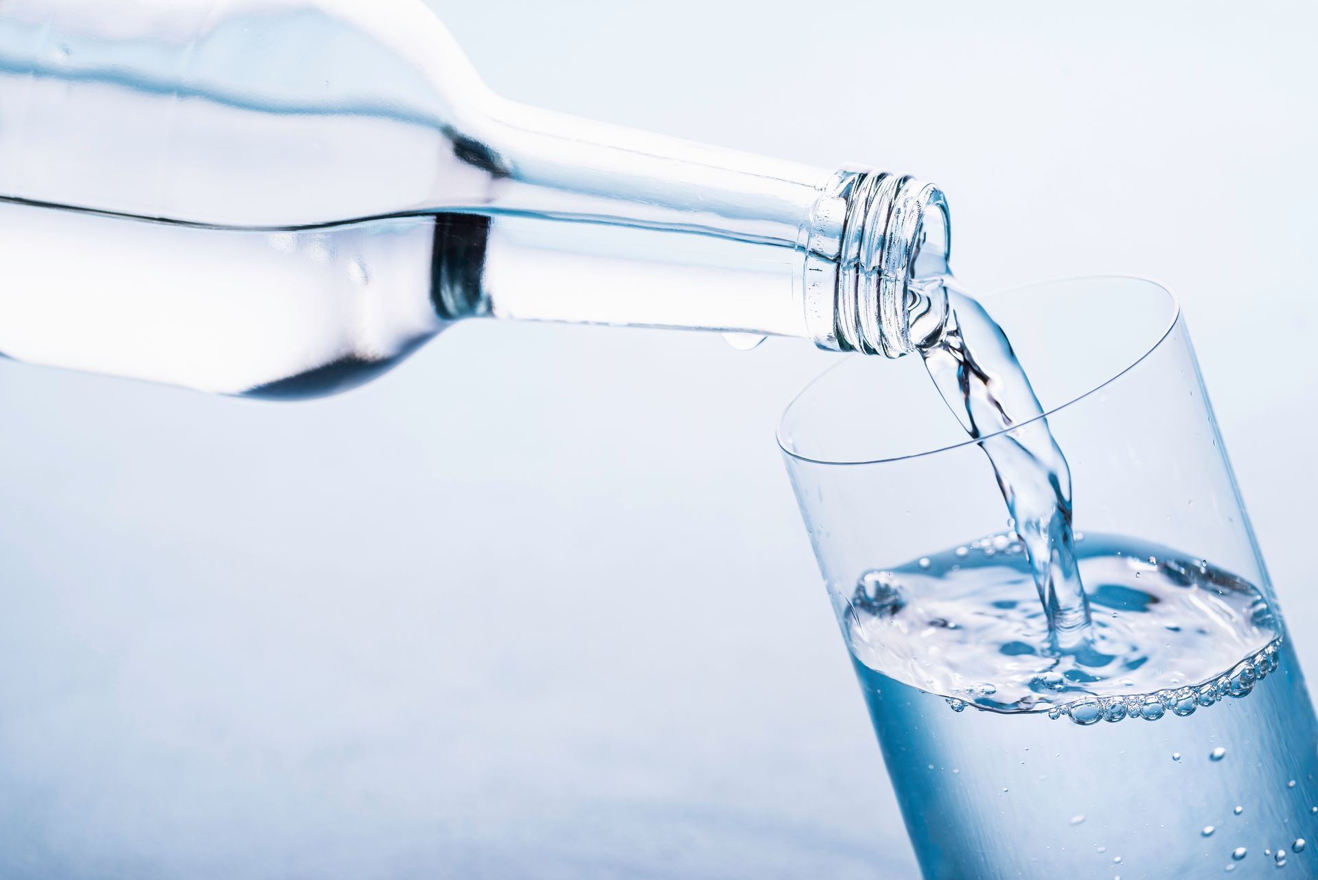 Water being poured from a glass bottle into a glass, with a blue background.