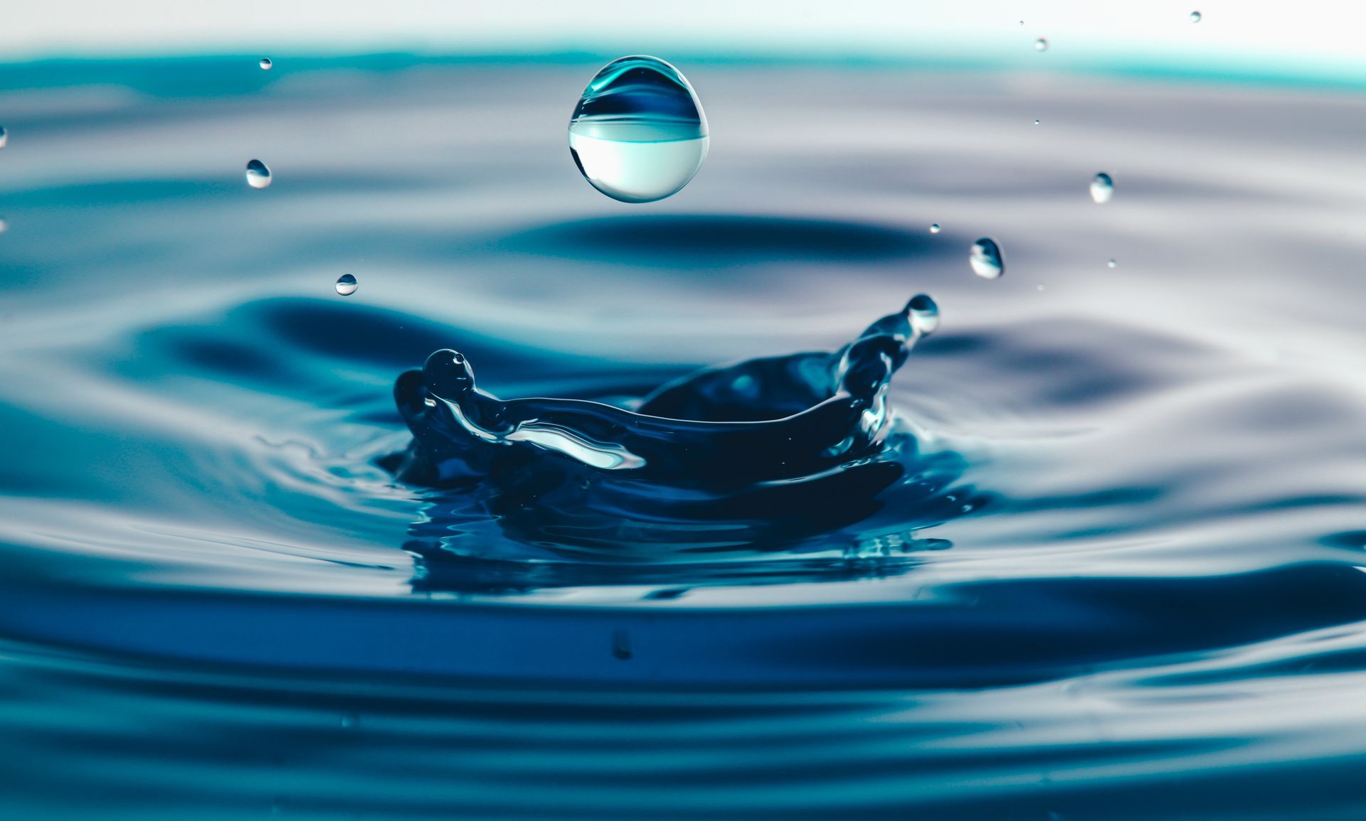 A water droplet falling into water, creating a crown-shaped splash. Blue hues.