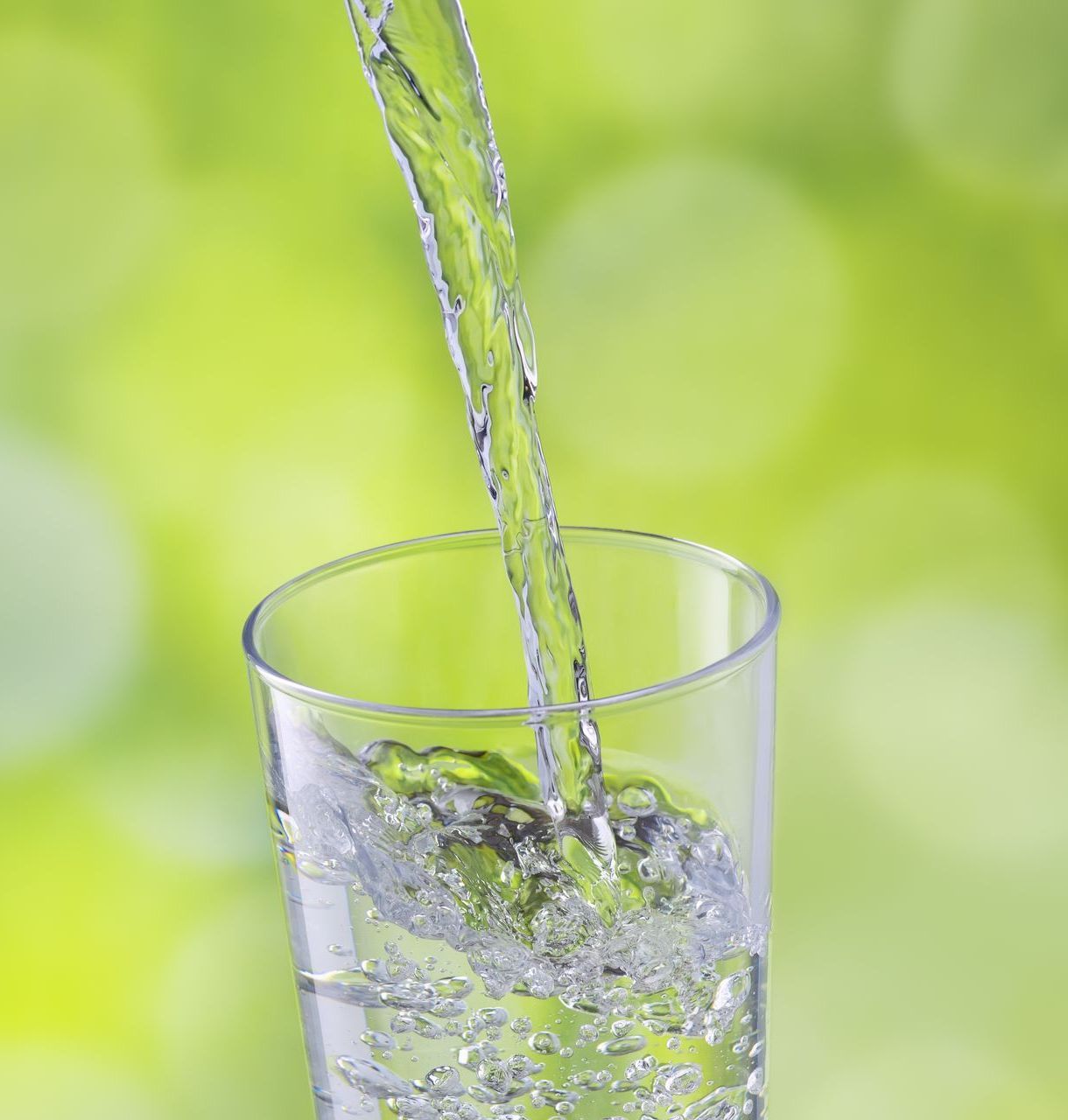 Water pouring into a clear glass, with a blurred green background.