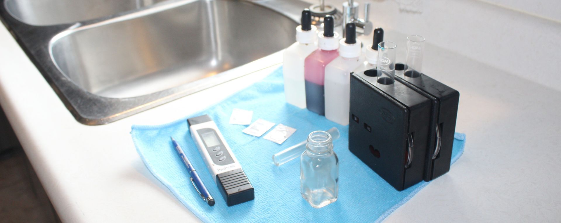 Various water testing equipment including bottles, a meter, and a sink.