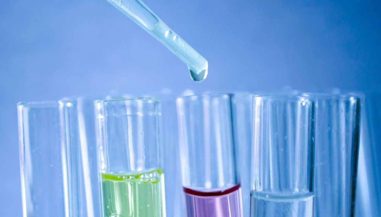 A dropper dispensing liquid into test tubes with colored contents in a laboratory setting.