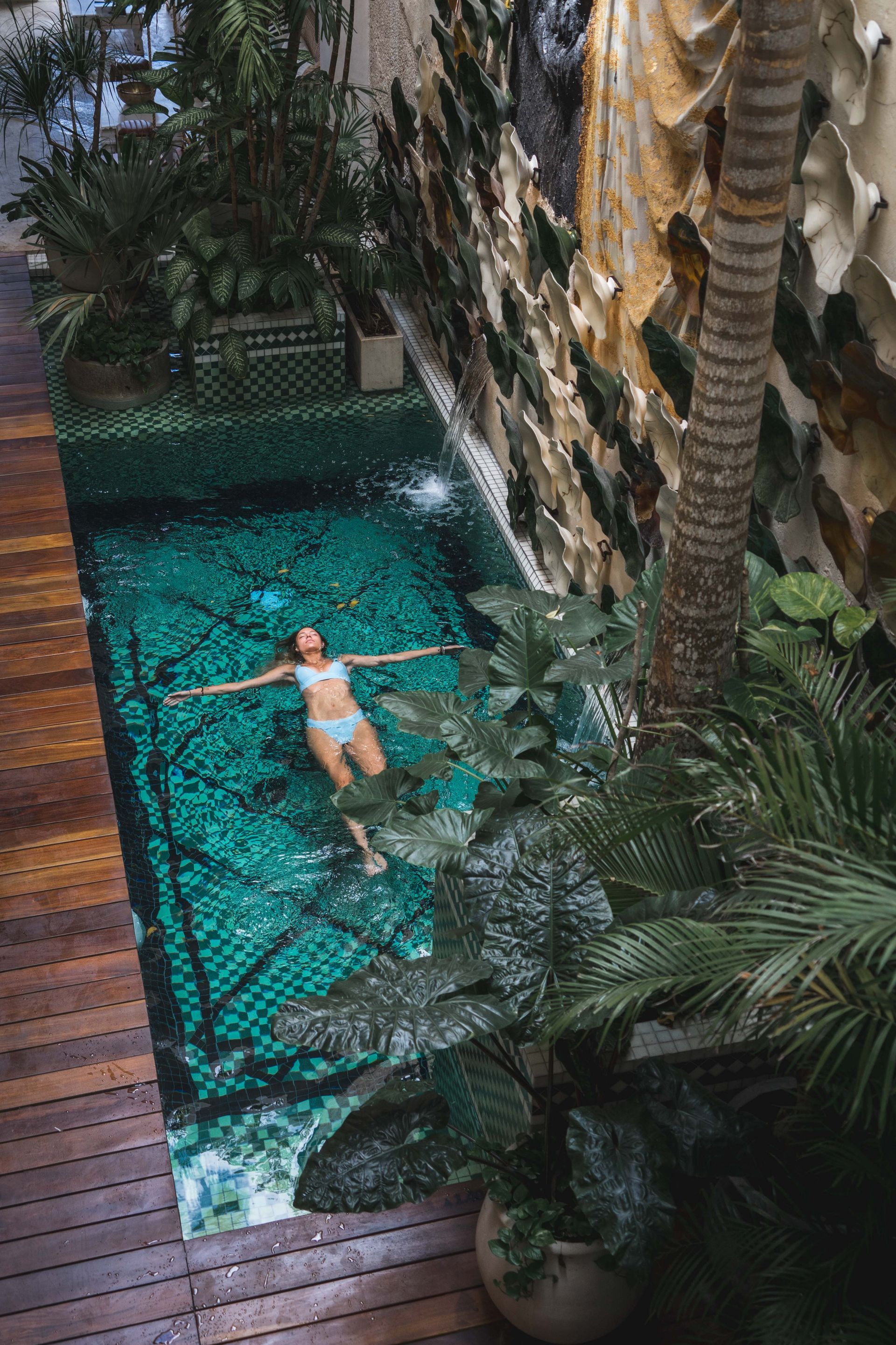 A woman is floating on her back in a swimming pool surrounded by plants.