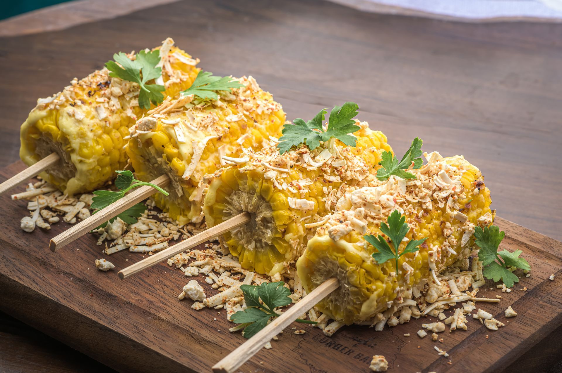 Mazorcas de maíz en palitos sobre una tabla de cortar de madera.