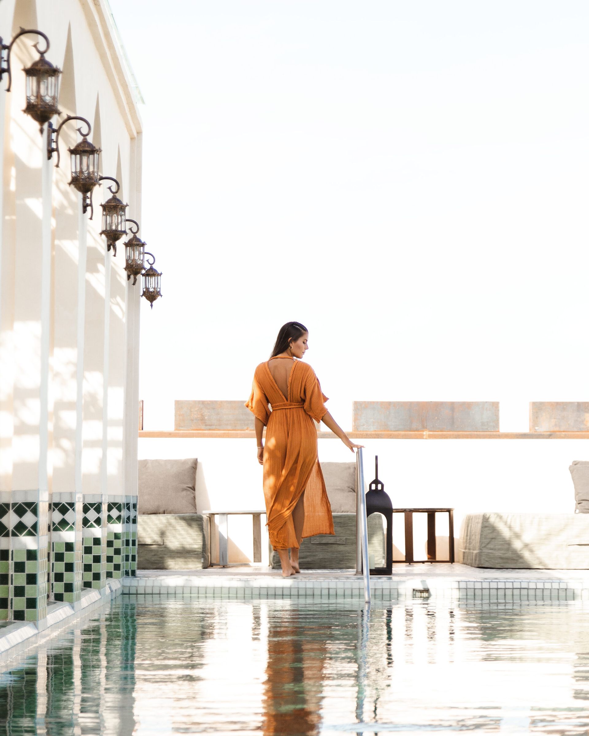 Una mujer con un vestido naranja está parada junto a una piscina.