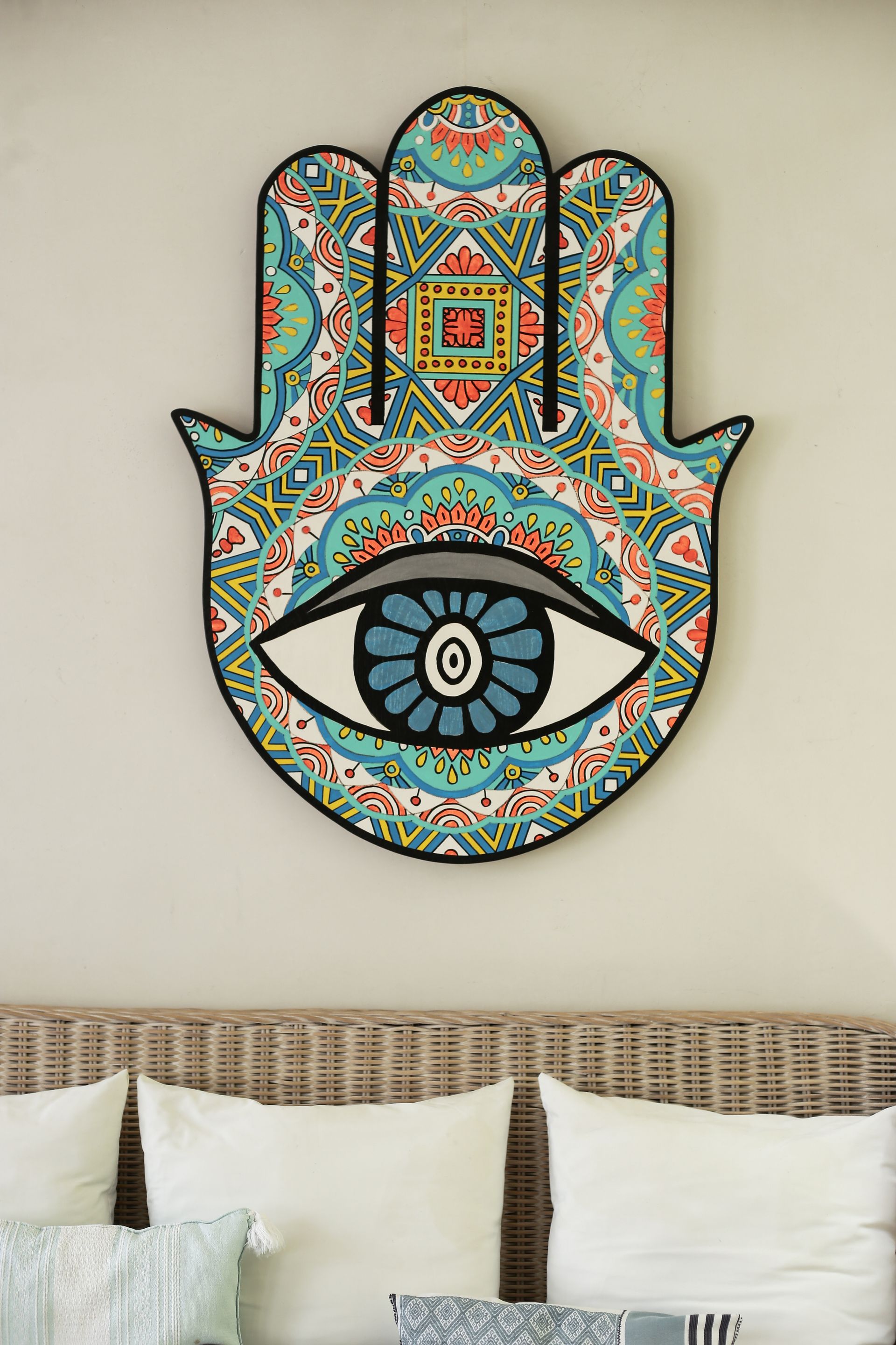 A hamsa hand with an eye on it is hanging on a wall above a couch.