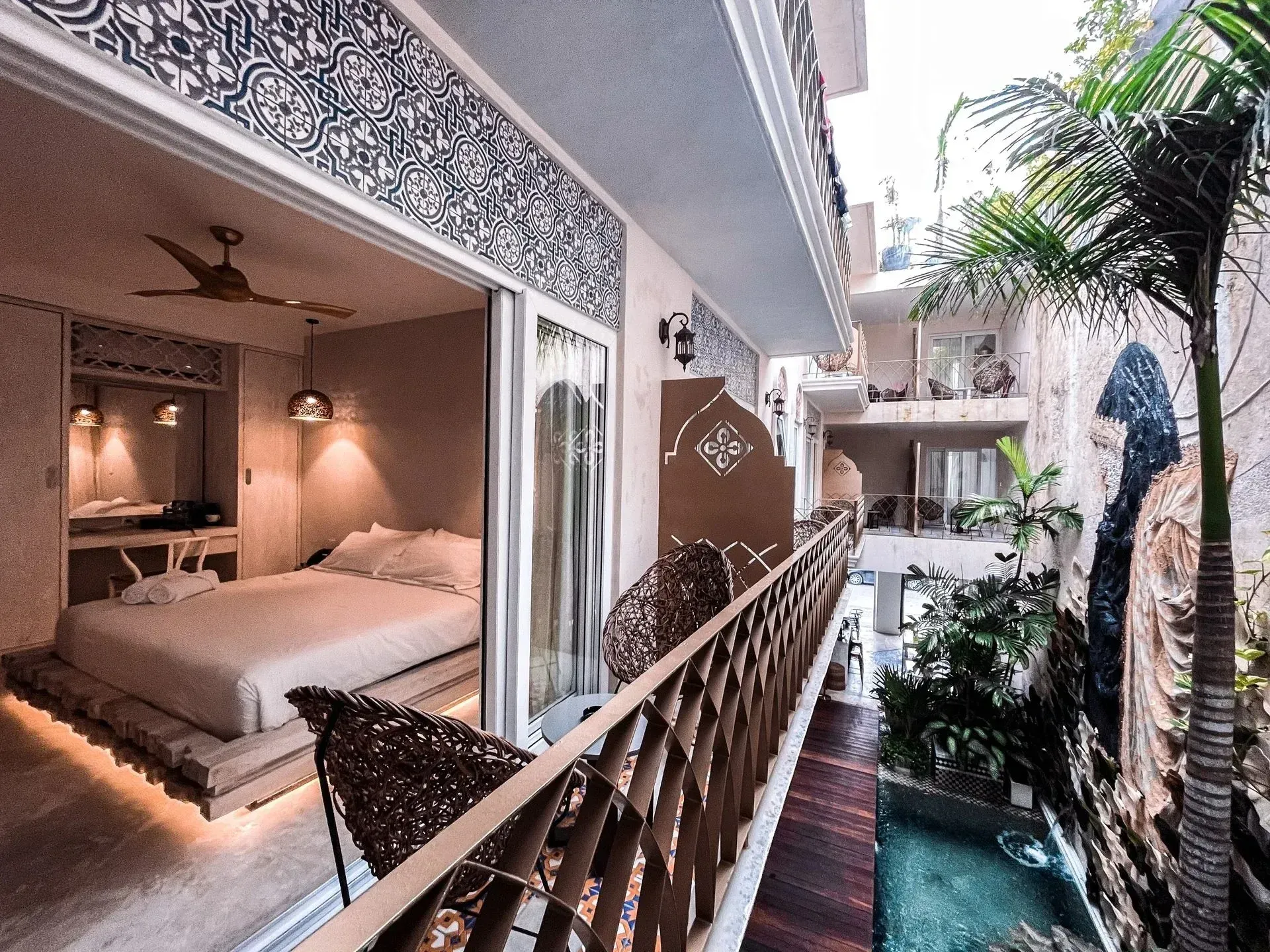 Bedroom with balcony overlooking a courtyard with a pool and palm trees. White walls with decorative blue tile.