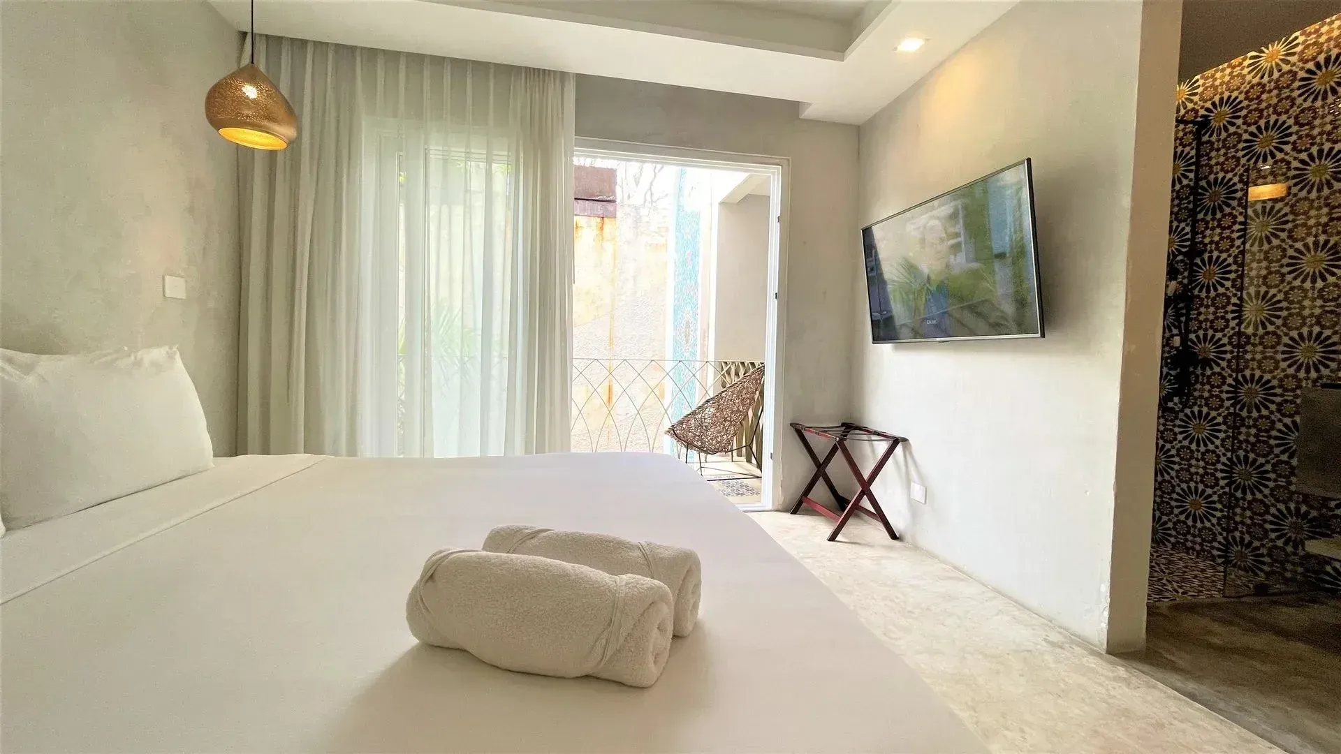 Bedroom with white bedding, TV, and balcony access. Rolled towels on bed.