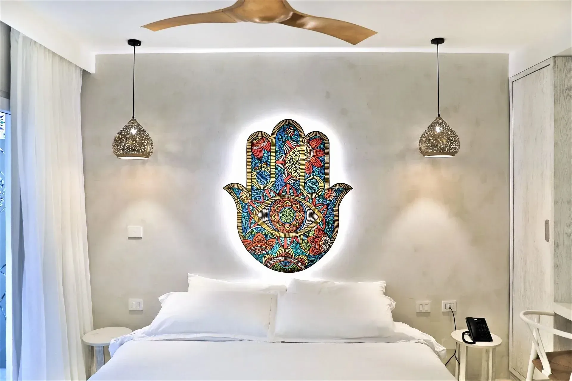 Bedroom with a bed, a decorative hamsa hand on the wall, and pendant lights.