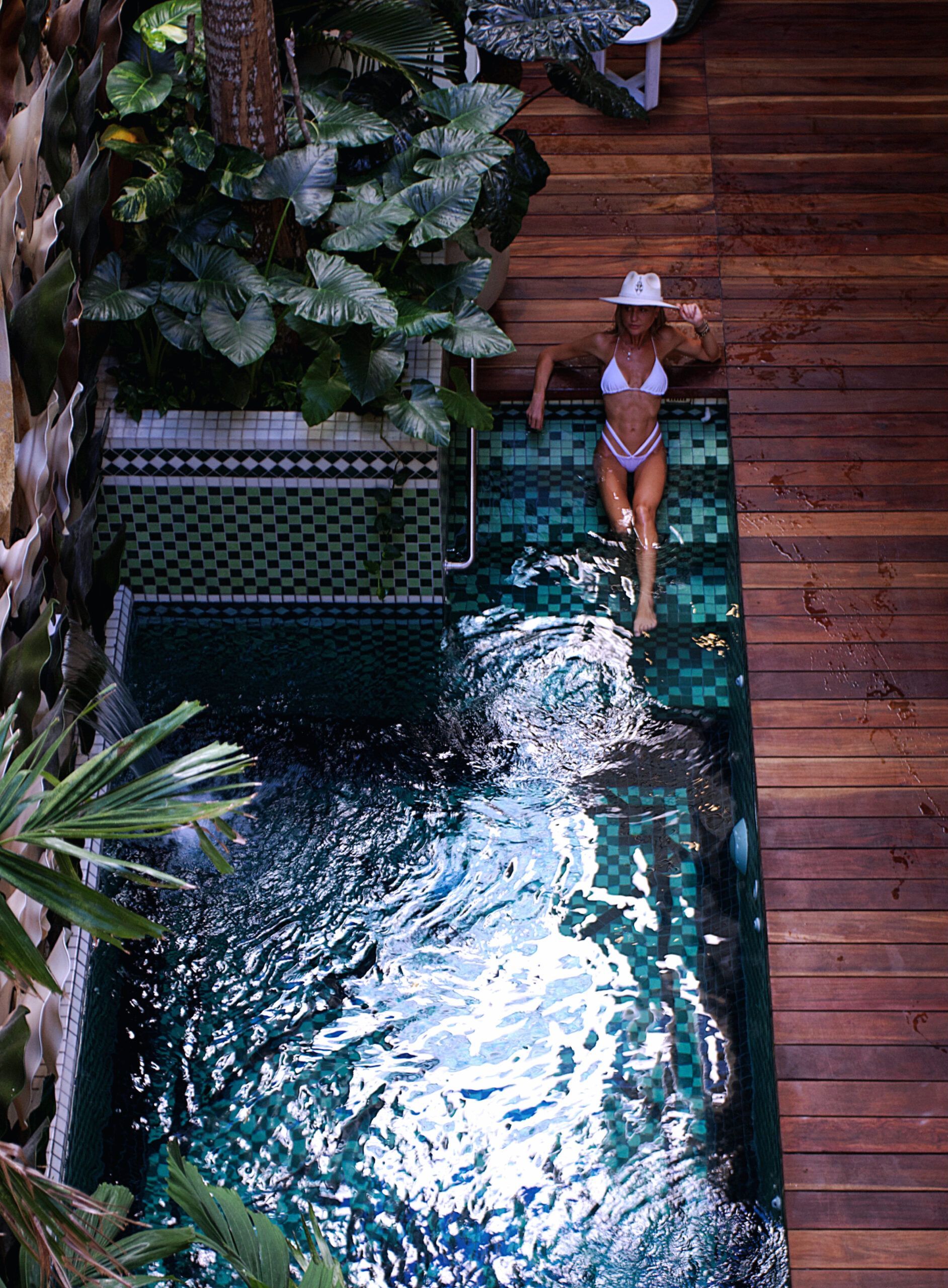 Una mujer en bikini está tumbada en una terraza de madera junto a una piscina.