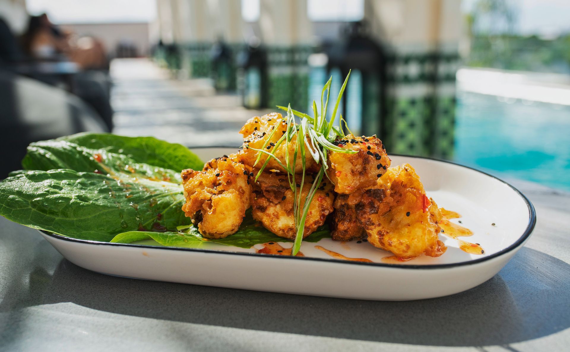 Un plato blanco cubierto con camarones fritos y lechuga sobre una mesa.
