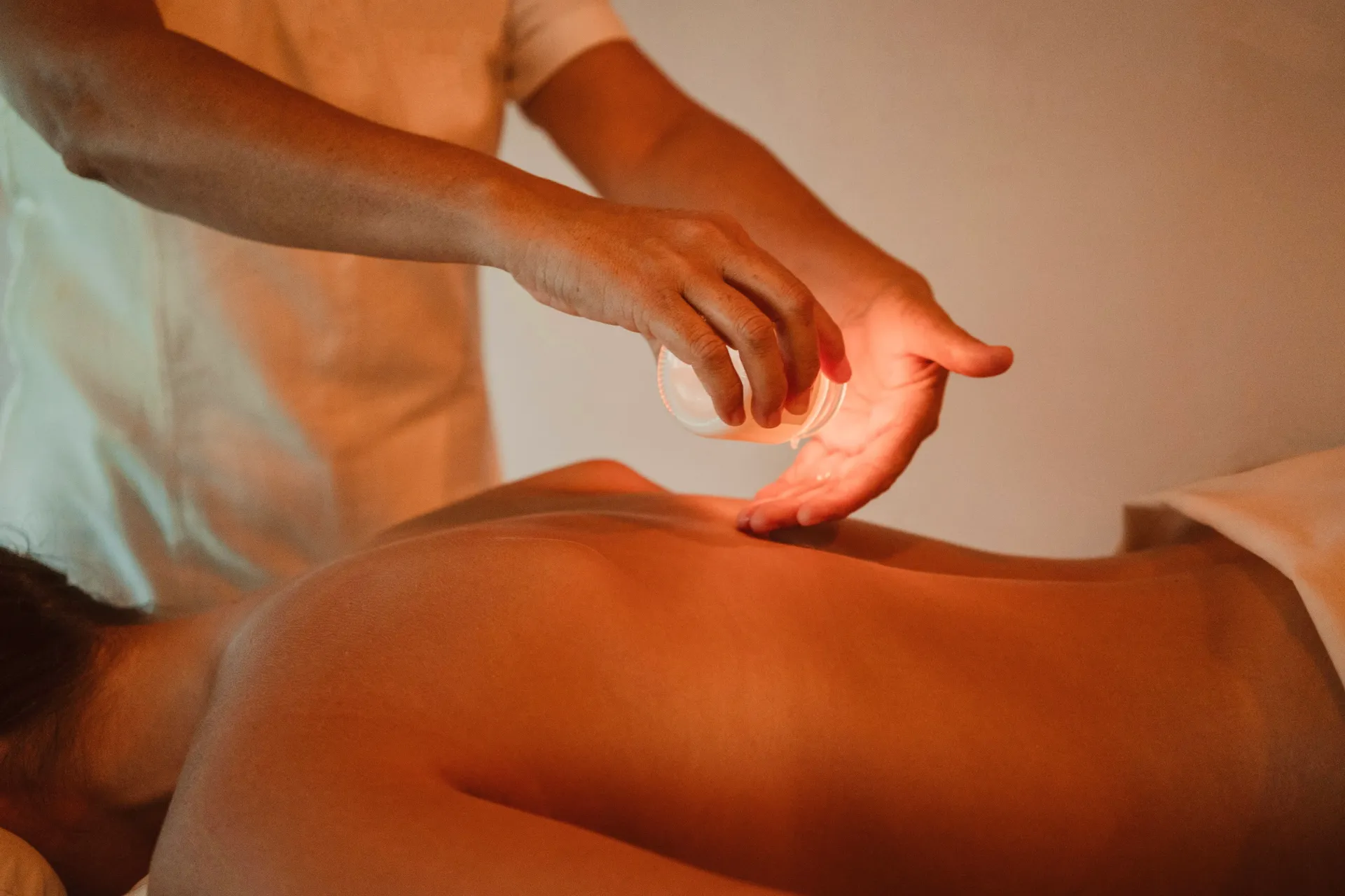 Persona recibiendo ventosas boca arriba. El terapeuta sostiene una copa de vidrio. Iluminación ambiental cálida.