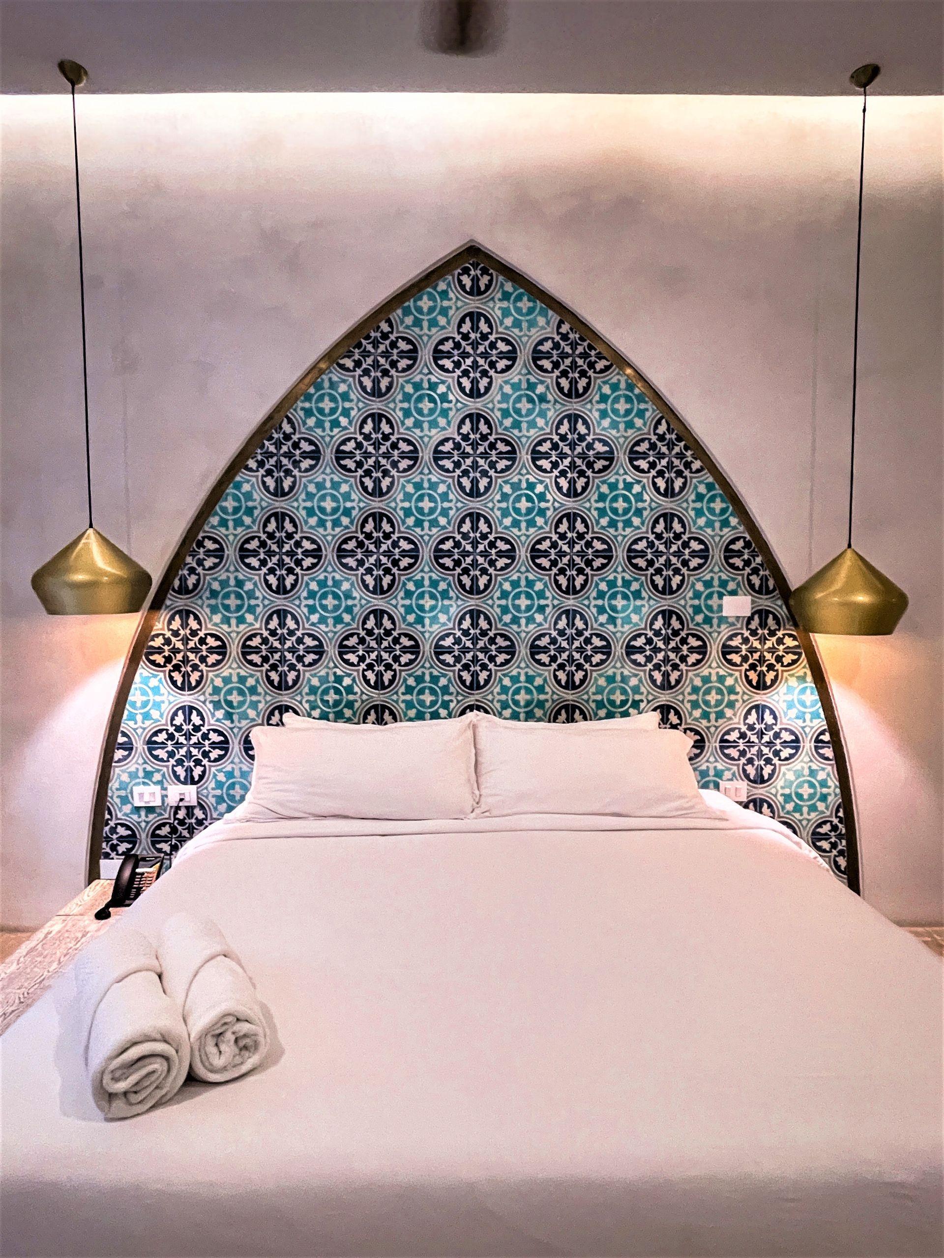 Una cama con cabecero estampado y dos toallas sobre la cama.