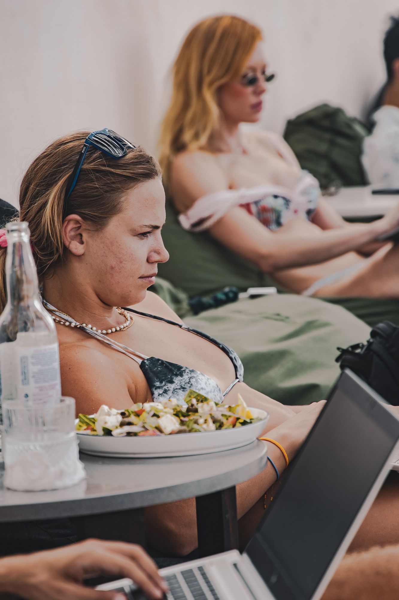 A woman in a bikini is sitting at a table with a laptop and a plate of food.