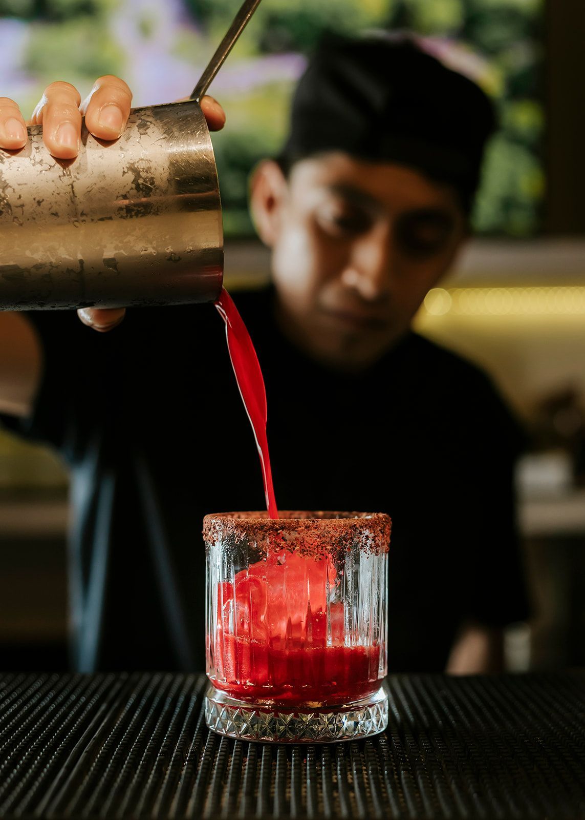 A bartender is pouring a red drink into a glass.