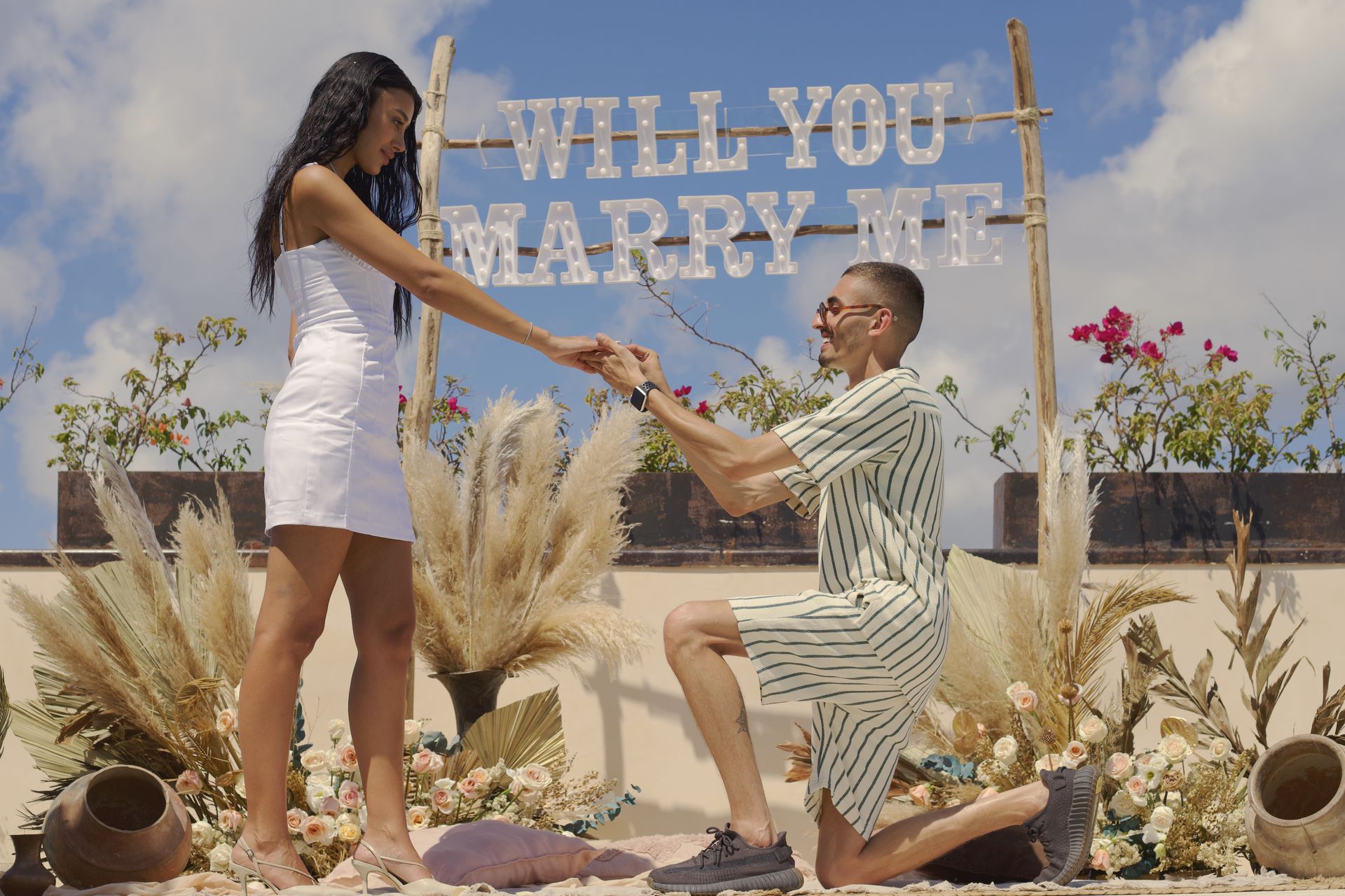 A man is kneeling down in front of a sign that says `` will you marry me ''.