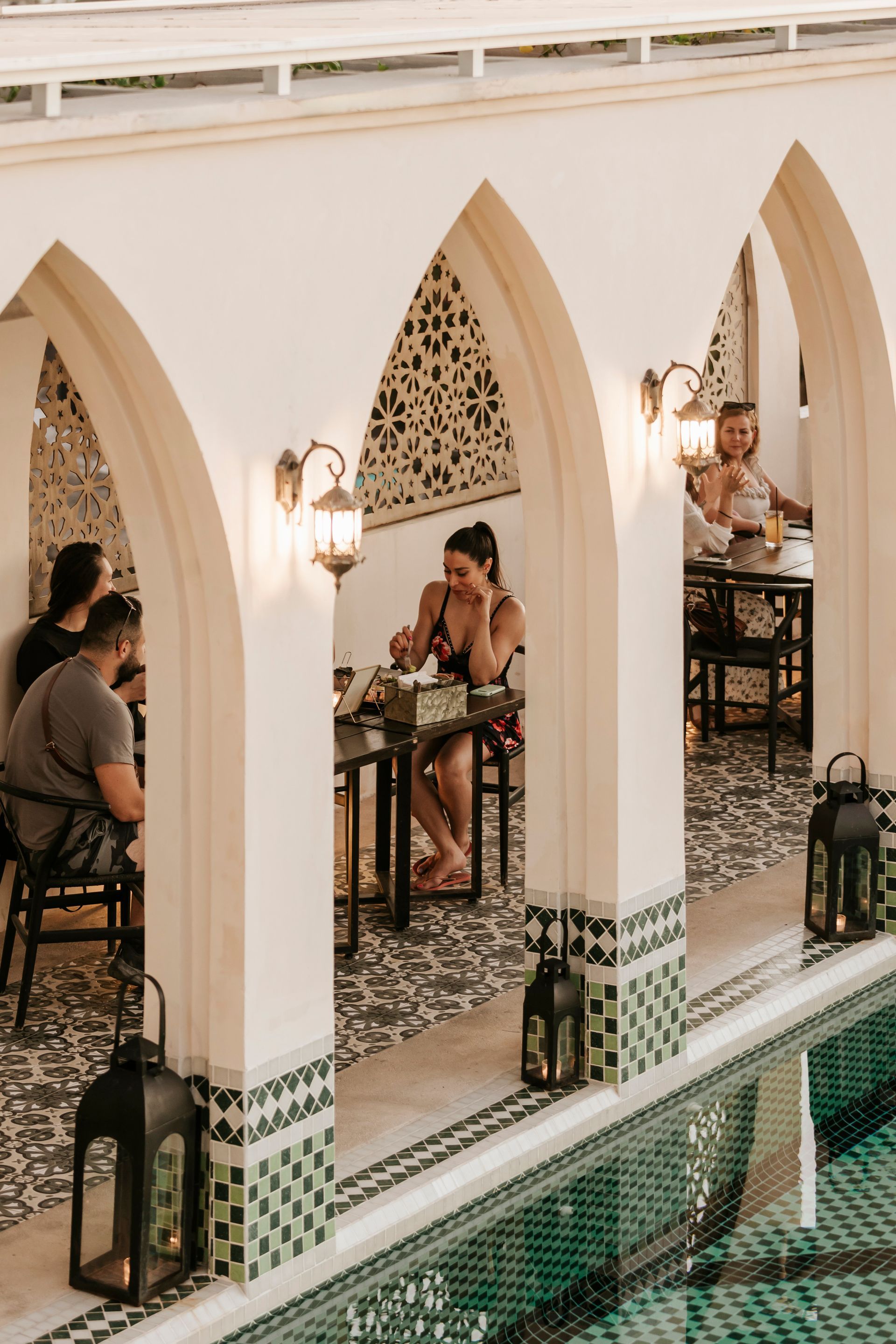 A group of people are sitting at tables next to a pool.